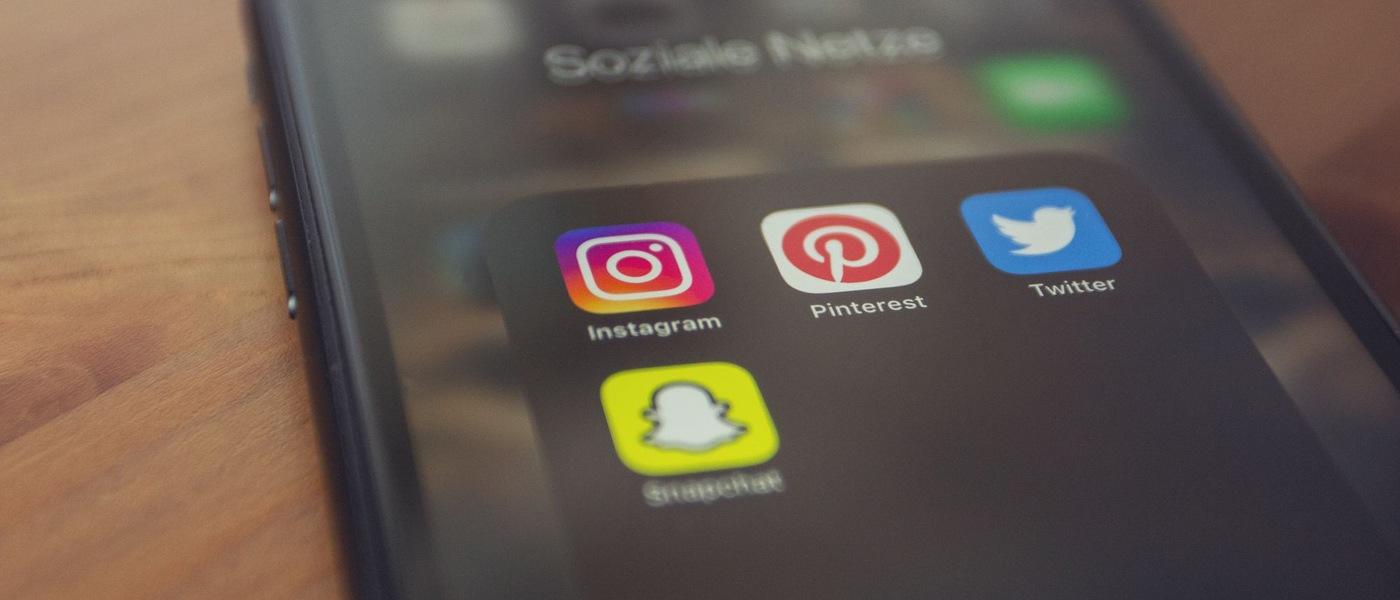 Smartphone posé sur une table en bois, avec un dossier d'icônes d'applications de réseaux sociaux à l'écran.