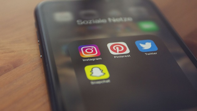Smartphone posé sur une table en bois, avec un dossier d'icônes d'applications de réseaux sociaux à l'écran.