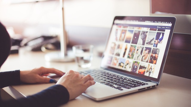Mains sur le clavier d'un ordinateur portable dont l'écran affiche une grille de photographies.