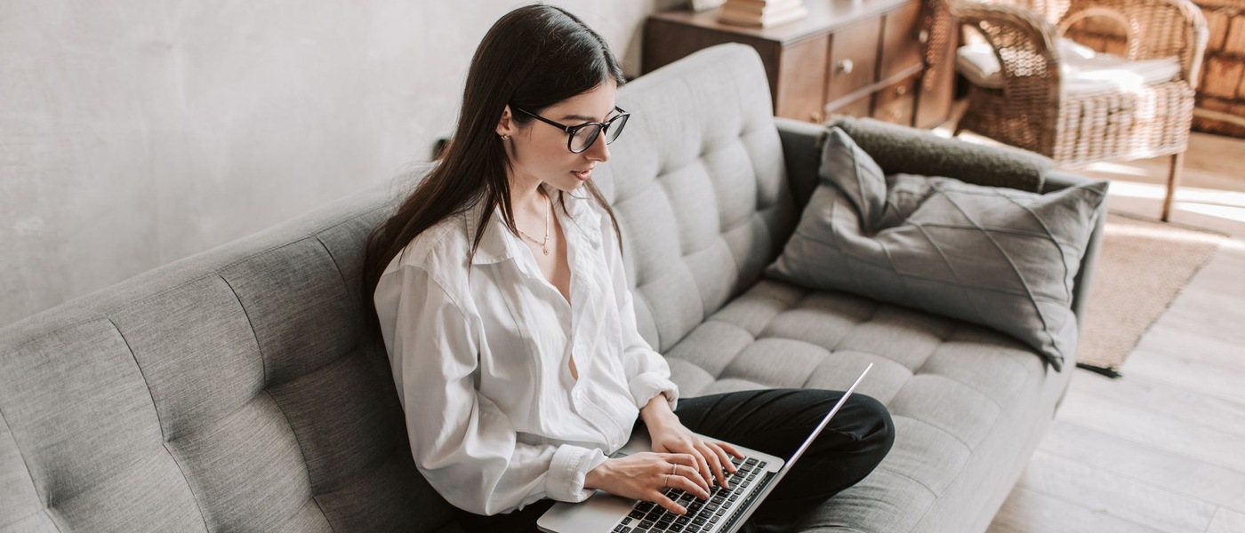 Femme assise sur un canapé gris, qui travaille sur un ordinateur portable.