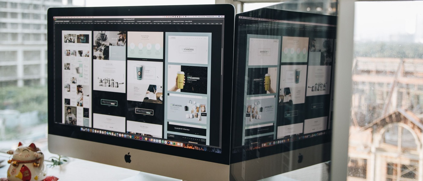 Écran d'iMac affichant des maquettes de pages web, à côté d'une figurine de chat porte-bonheur et d'une fenêtre.