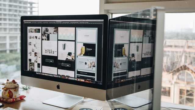 Écran d'iMac affichant des maquettes de pages web, à côté d'une figurine de chat porte-bonheur et d'une fenêtre.