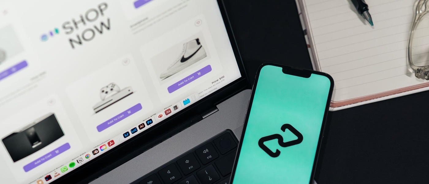 Ordinateur portable affichant une page de boutique en ligne, avec un smartphone posé sur le clavier et un carnet à côté.