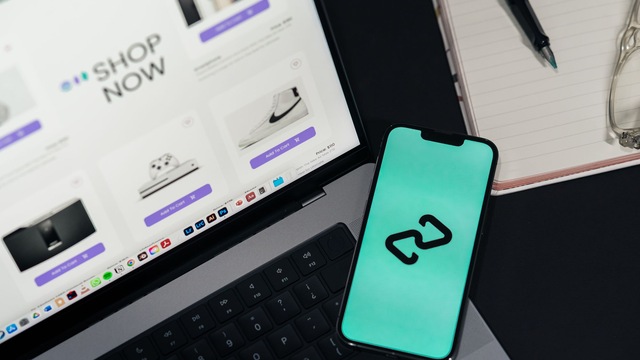 Ordinateur portable affichant une page de boutique en ligne, avec un smartphone posé sur le clavier et un carnet à côté.