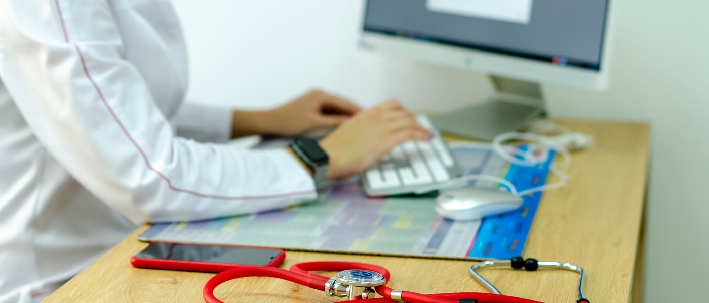 Mains sur un clavier, blouse blanche et stéthoscope rouge.