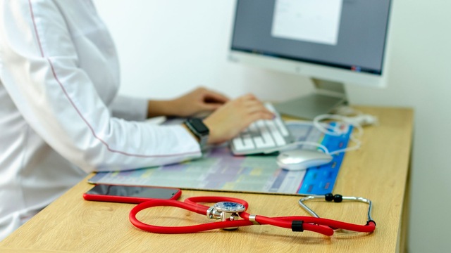 Mains sur un clavier, blouse blanche et stéthoscope rouge.